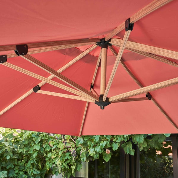 Unteransicht eines Sonnenschirms mit Holzgestell und rotem Stoffbezug im Garten vor Pflanzen.