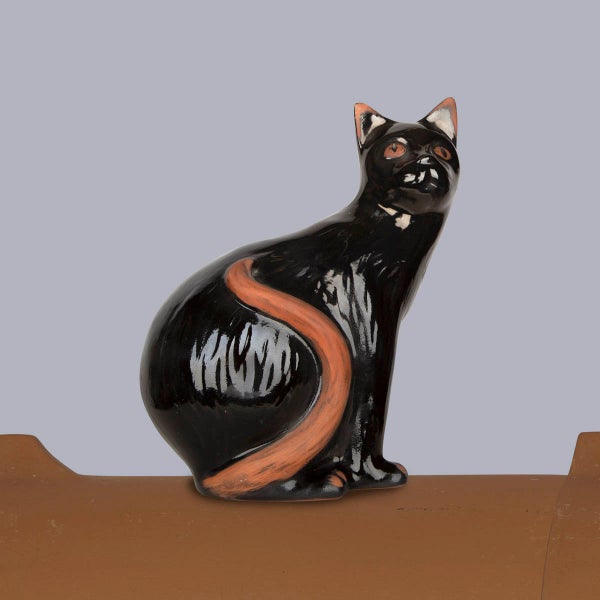 Firstfigur aus glasiertem Ton in Form einer sitzenden schwarzen Katze mit terrakottafarbenen Details.