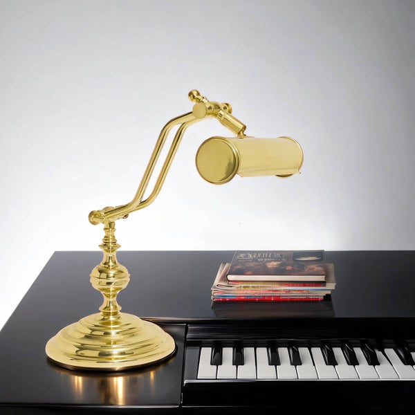 Goldene Klavierleuchte auf einem schwarzen Klavier mit Notenbüchern.