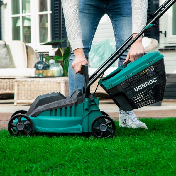 Eine Person hebt den Grasfangkorb eines Vonroc Rasenmähers an, während sie auf einem Rasen im Garten steht.