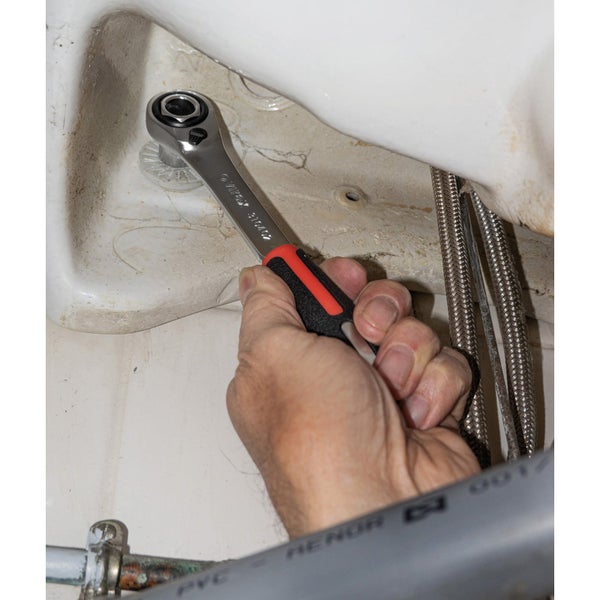 Eine Hand benutzt einen Ratschenschlüssel an einem Toilettenbecken.