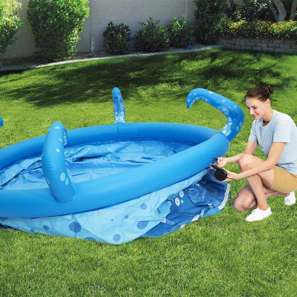 Eine Frau pumpt einen blauen aufblasbaren Kinderpool mit Tentakeln auf einer Rasenfläche mit einer elektrischen Pumpe auf.