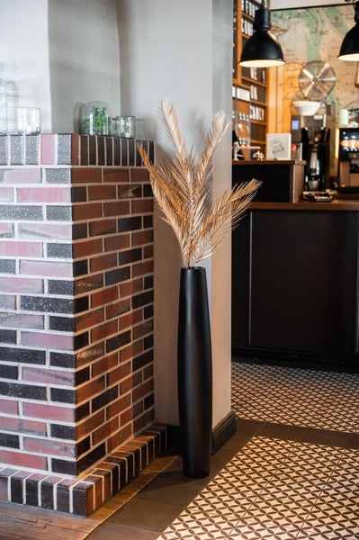 Schwarze Vase mit goldenen künstlichen Palmwedeln vor einer Ziegelwand.