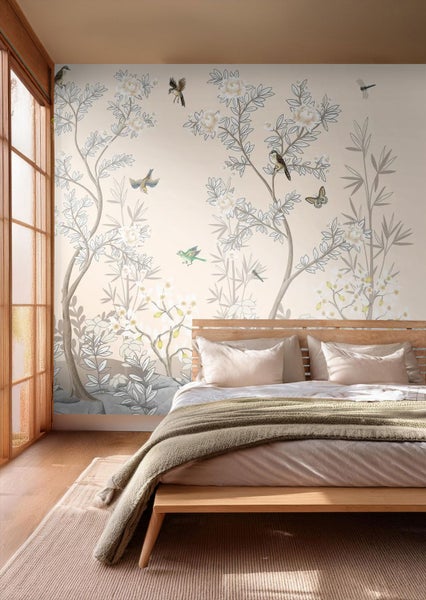 Vliestapete mit floralem Muster, Bäumen, weißen Blüten und Vögeln in einem hellen Schlafzimmer mit Holzbett.