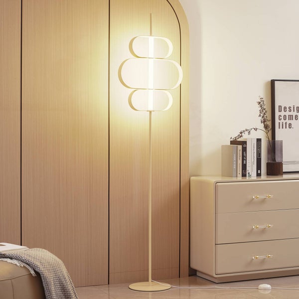 Moderne Stehleuchte mit drei ovalen Leuchtelementen in einem hellen, organisierten Raum neben einer Kommode vor einer Wand in Holzoptik.