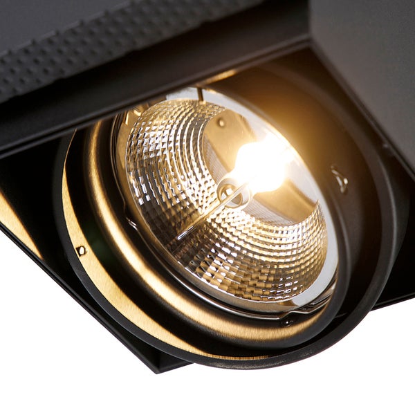 Nahaufnahme eines eingeschalteten LED-Strahlers mit facettiertem Reflektor und schwarzem Metallgehäuse.