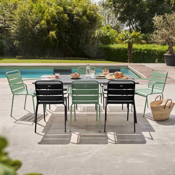 Gartensitzgruppe bestehend aus einem großen dunklen Tisch und acht Metallstühlen in Mintgrün und Schwarz auf einer Terrasse am Pool.