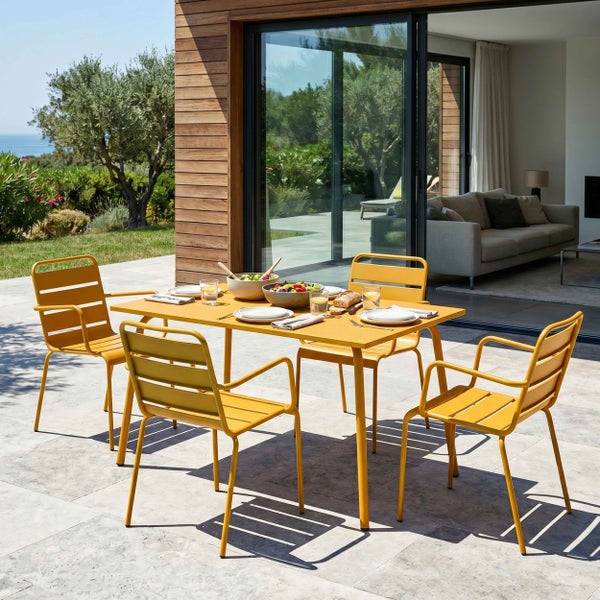 Gartensitzgruppe aus gelbem Metall mit Tisch und vier Stühlen auf einer Steinterrasse vor einem modernen Haus mit Glasfront.