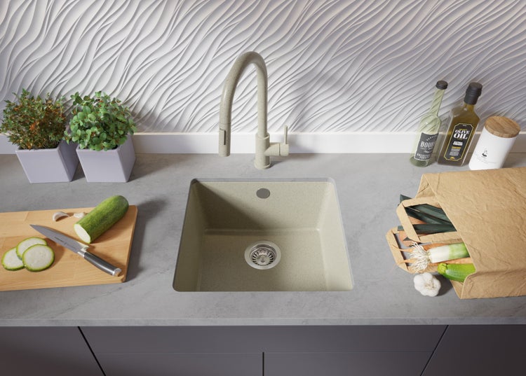 Küchenspüle aus Verbundmaterial mit Armatur, Schneidebrett, Gemüse und Dekoration auf einer Küchentheke.