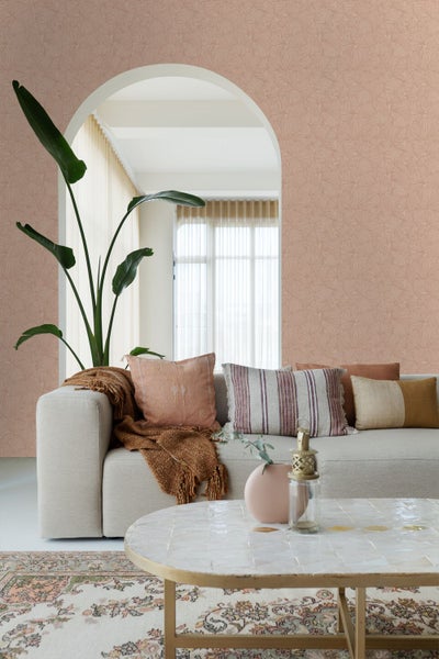 Wohnzimmer mit Vliestapete mit Fächermotiv, beigefarbenem Sofa mit Dekokissen, Pflanze und Couchtisch in einem hellen und stilvollen Ambiente.