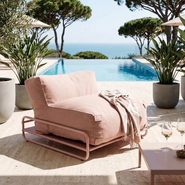 Moderner Loungesessel mit Metallgestell und Textilpolster auf einer hellen Terrasse an einem Pool mit Meerblick und Pflanzen.