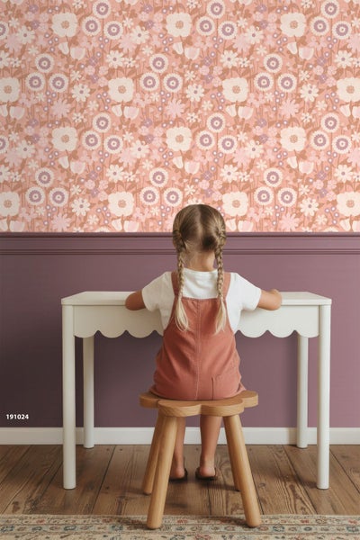 Kinderzimmer mit floraler Vliestapete, weißem Schreibtisch mit Wellenkante und Holzschemel vor einer halbhoch lila gestrichenen Wand.