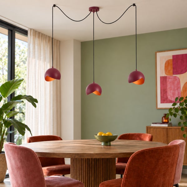 Moderne dreiflammige Pendelleuchte mit halbkugelförmigen Metalllampenschirmen über einem runden Esstisch in einem hellen Esszimmer.