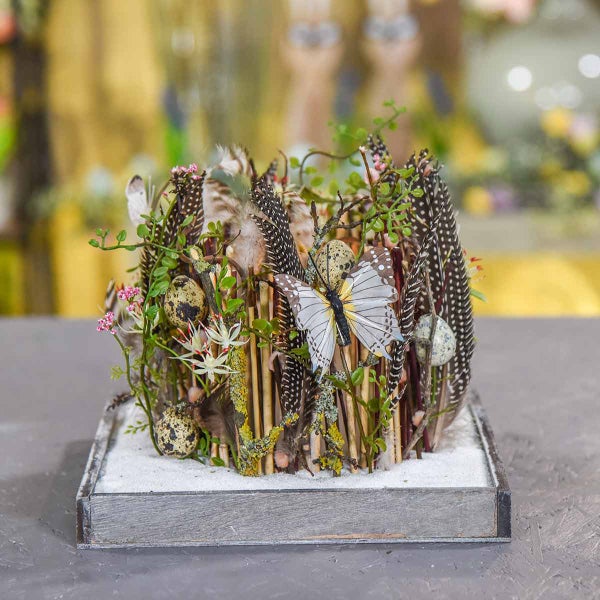 Dekoratives Gesteck mit Federn, Eiern und Schmetterling auf einem Holztablett