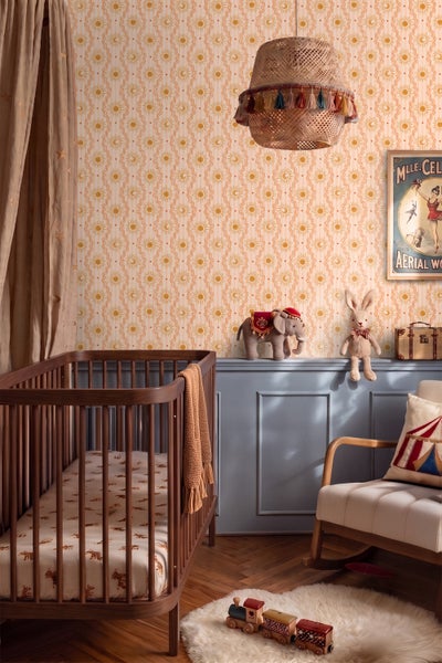 Kinderzimmer mit Gitterbett aus dunklem Holz, Tapete mit Sonnen- und Mondmotiven, Wandpaneelen und Schaukelstuhl.