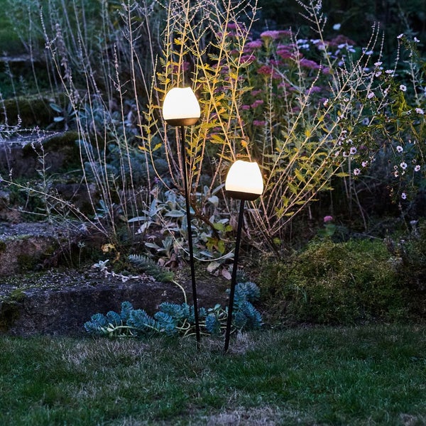 Zwei Gartenleuchten mit Erdspieß beleuchten einen Garten bei Dämmerung.