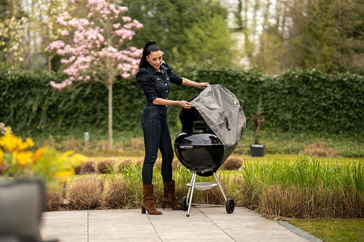 Frau entfernt Abdeckung von Kugelgrill im Garten.