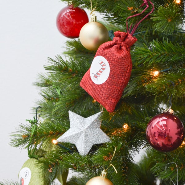 Weihnachtsbaum mit Adventskalender-Beuteln, Christbaumkugeln, Sternanhänger und Lichterkette als festliche Dekoration.