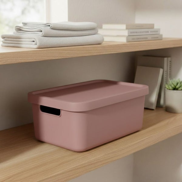 Aufnahme eines Regals mit einer rosa Aufbewahrungsbox mit Deckel, gefalteten Textilien und Büchern.