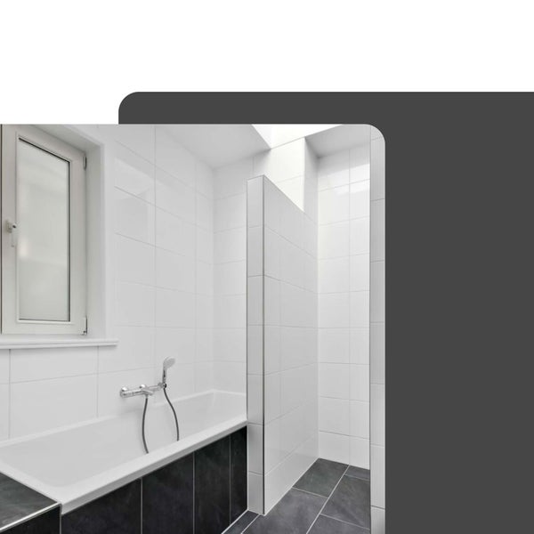 Helles, modernes Badezimmer mit weißer Badewanne, dunklen Fliesen und einem begehbaren Duschbereich mit weißen Wandfliesen.