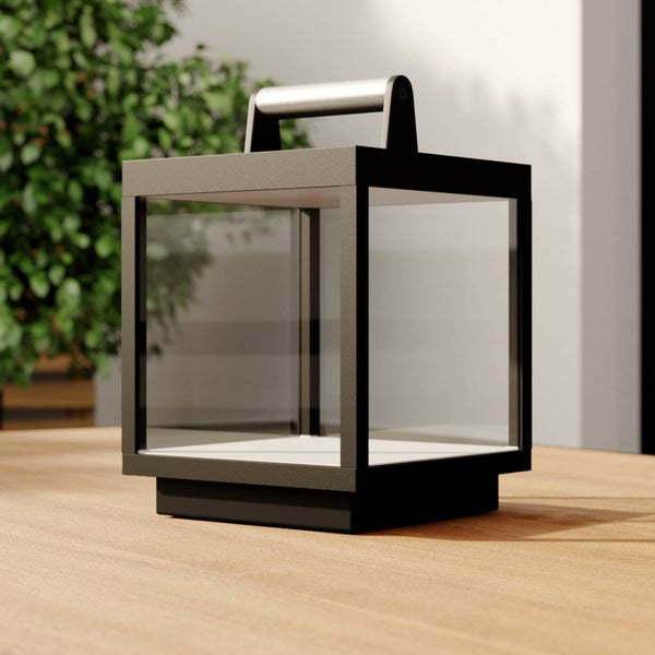 Würfelförmige Außenlaterne mit dunklem Metallrahmen, Glasfenstern und silbernem Tragegriff auf einem Holztisch.