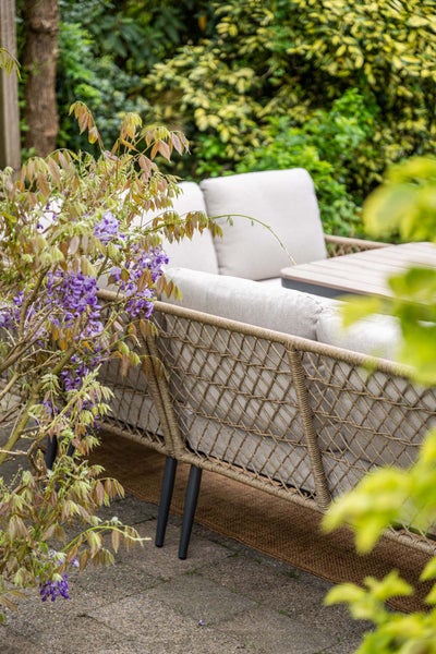 Garten-Lounge-Sofa mit dekorativem Seilgeflecht und hellen Kissen auf einer Terrasse inmitten von Pflanzen.