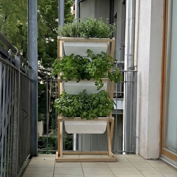 Vertikaler Kräutergarten aus Holz mit drei Etagen und weißen Pflanzkästen auf einem Balkon.
