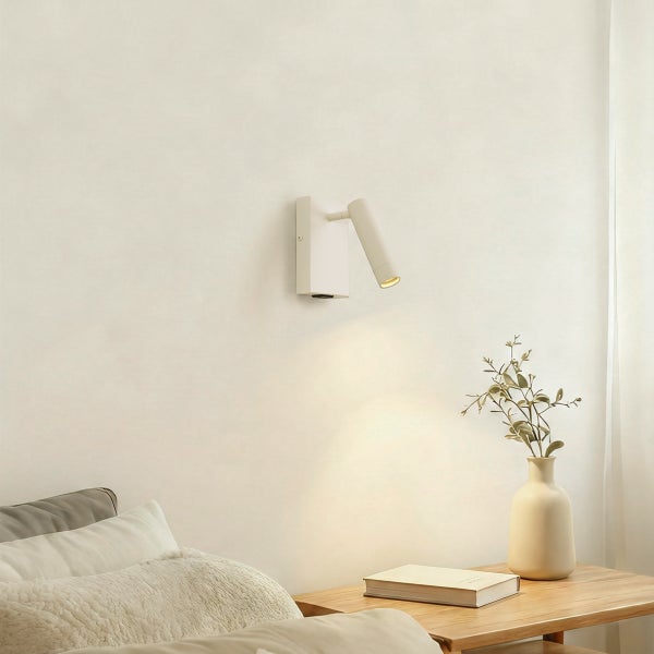 Moderne weiße Wandleuchte mit verstellbarem Strahler in einem hellen Schlafzimmer über einem hölzernen Nachttisch.
