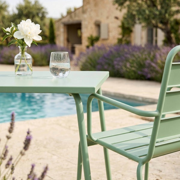 Grüner Gartentisch und Gartenstuhl aus Metall im Garten am Pool mit Lavendel und Steinfassade im Hintergrund.
