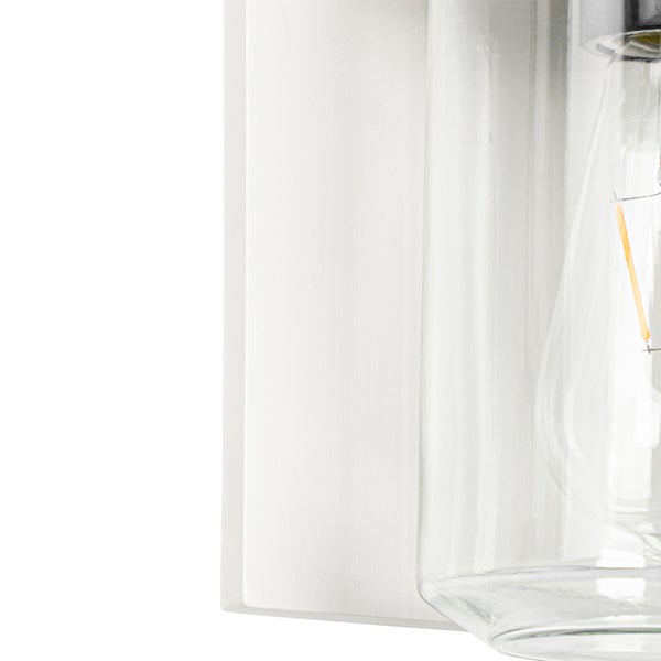 Nahaufnahme einer Wandleuchte mit weißem Sockel und klarem Glaszylinder, in dem ein LED-Filament-Leuchtmittel sichtbar ist.