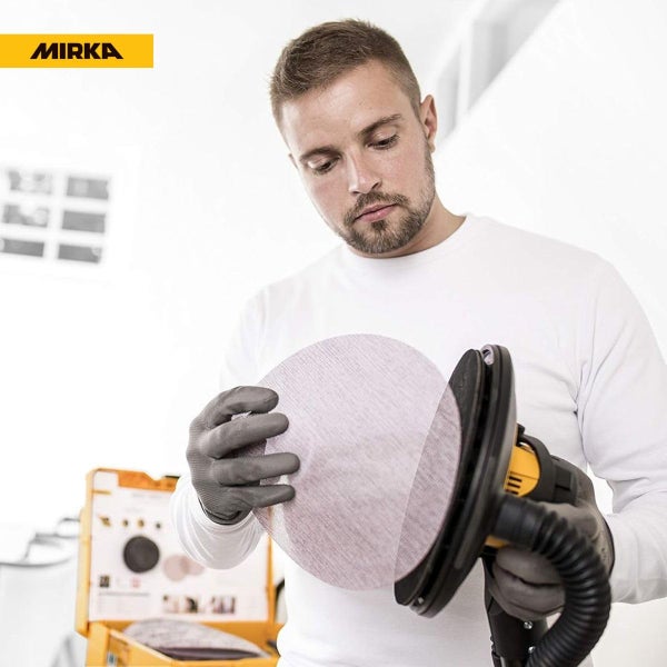 Handwerker befestigt ein kreisförmiges Schleifgitter an einem Exzenterschleifer, Mirka Logo oben links.