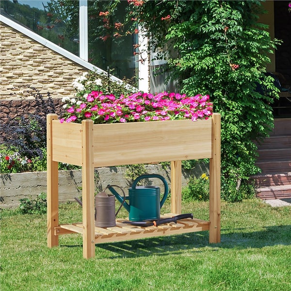 Hochbeet aus Holz mit Blumen, Gießkannen und Gartengeräten im Garten