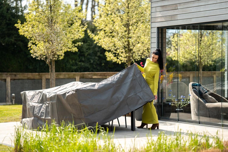Eine Frau deckt eine Gartentischgruppe mit einer Schutzhülle ab.