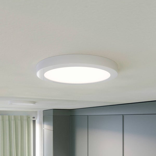 Runde LED-Deckenleuchte in Weiß, flaches Design, an einer Zimmerdecke montiert, im Hintergrund graue Schränke und helle Vorhänge.