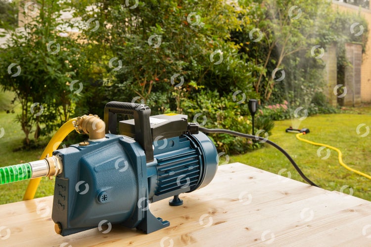 Gartenwasserpumpe mit Schläuchen auf Holztisch vor Garten