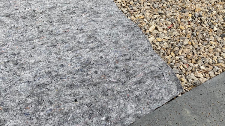 Graues Unkrautvlies neben einer Schicht aus hellem Kies und einer Betonkante.