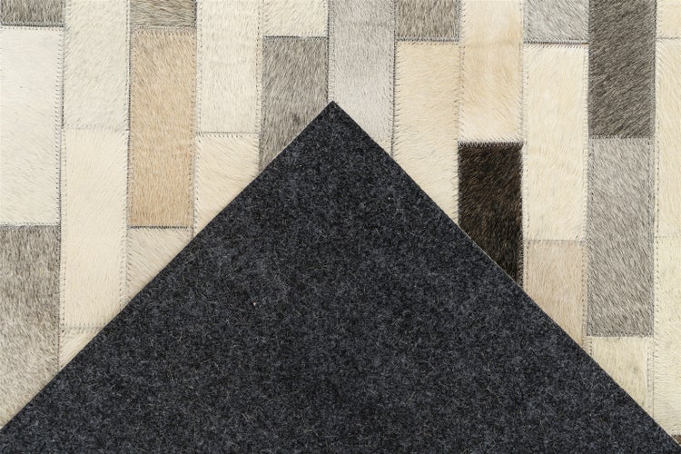 Patchwork-Teppich aus Kuhfell-Rechtecken mit sichtbaren Nähten und dunkler Filzunterseite.