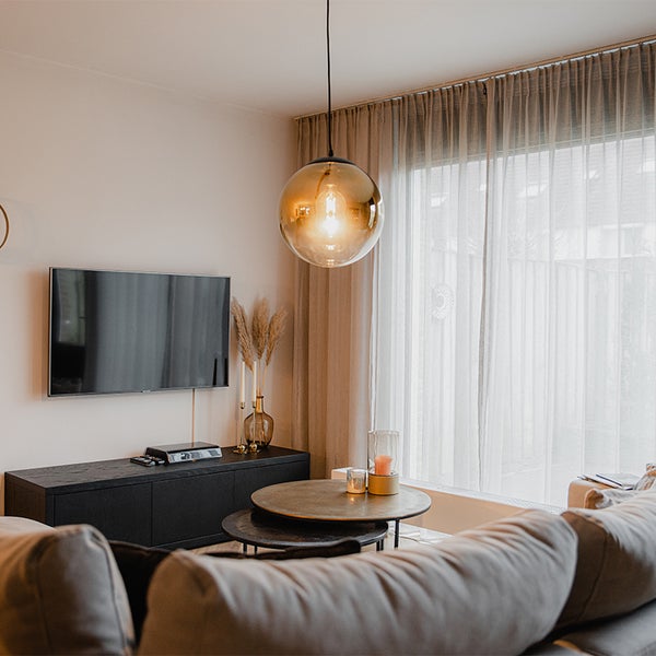 Wohnzimmer mit Fernseher, Couchtisch, Hängelampe und Vorhängen für eine gemütliche Atmosphäre