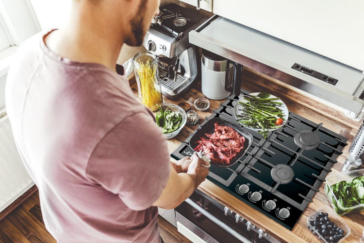 Person brät Fleisch in einer Pfanne auf einem modernen Gaskochfeld in einer organisierten Küche.