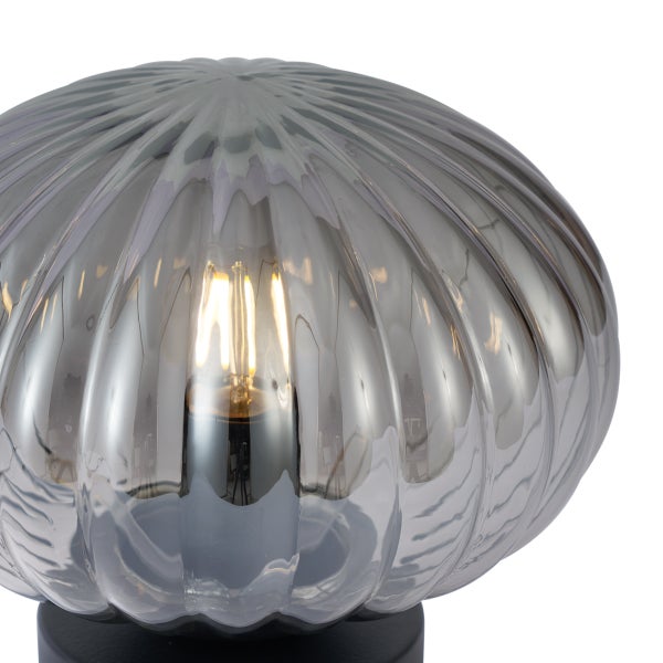 Tischleuchte mit geriffeltem Schirm aus Rauchglas, schwarzem Standfuß und sichtbarem Leuchtmittel.