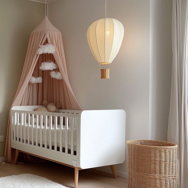 Helles Kinderzimmer mit weißem Gitterbett aus Holz, rosa Betthimmel mit Wolkendekoration und Pendelleuchte in Heißluftballon-Form.