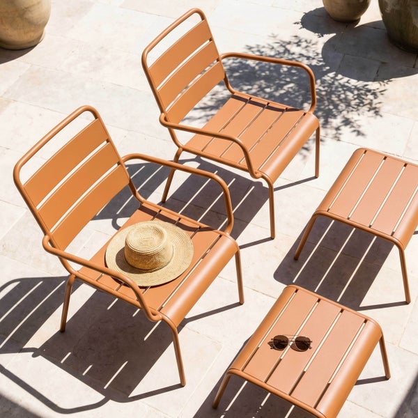 Modernes Gartenmöbel-Set aus Metall mit zwei lamel-lierten Sesseln und zwei passenden Beistelltischen auf einer Steinterrasse.