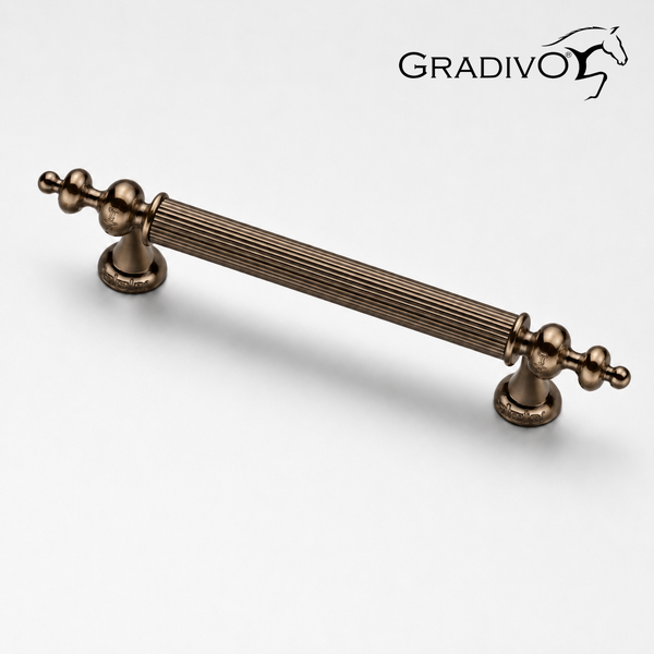 Dekorativer Möbelgriff in Bronze-Optik mit geriffeltem Mittelstück und verzierten Enden. Gradivo Logo.