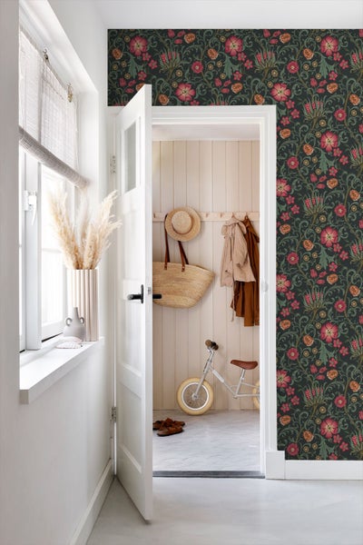 Helles Zimmer mit gemusterter Blumentapete, weißer Tür und Flur mit Holzpaneelen, Garderobe und Kinderlaufrad.
