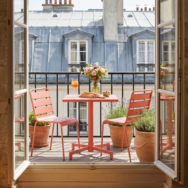 Modernes Balkon-Set mit Metallstühlen, einem quadratischen Mittelfußtisch und Terrakotta-Pflanztöpfen auf einem Holzboden mit Blick über Hausdächer.