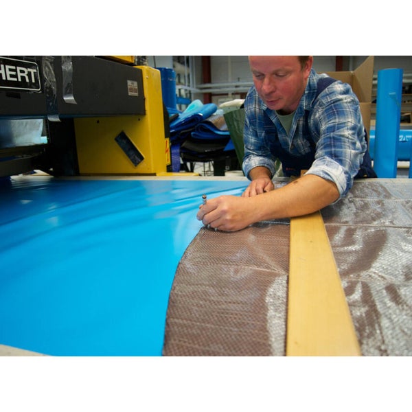 Ein Handwerker schneidet mit einem Werkzeug ein blaues Material an einer Werkbank zu.