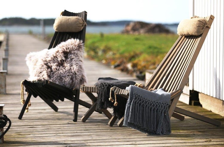 Zwei hölzerne Deckchairs mit Kissen und Decken auf einem Holzsteg am Wasser.