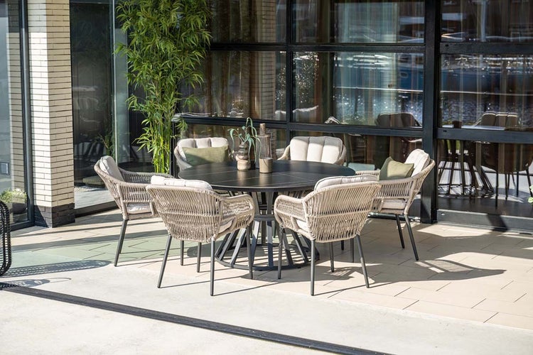 Moderne Terrassenessgruppe mit einem runden Tisch und vier Stühlen aus Geflecht mit Sitzpolstern auf einer gefliesten Terrasse.