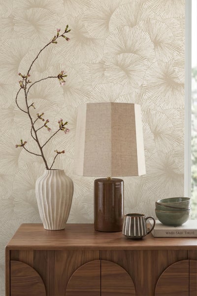 Vliestapete mit Ginkgo-Blattmuster an einer Wand hinter einem Holz-Sideboard mit Tischlampe und Keramikvase.