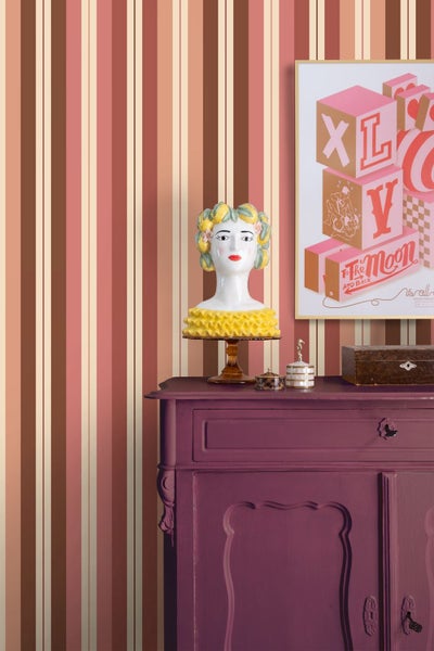 Gestreifte Vliestapete mit vertikalen Streifen in Braun und Creme hinter einer violetten Kommode mit dekorativer Büste.